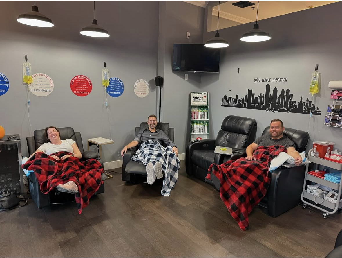 Three clients relaxing in leather recliners with IV drips inside the IV League Hydration South Boston clinic