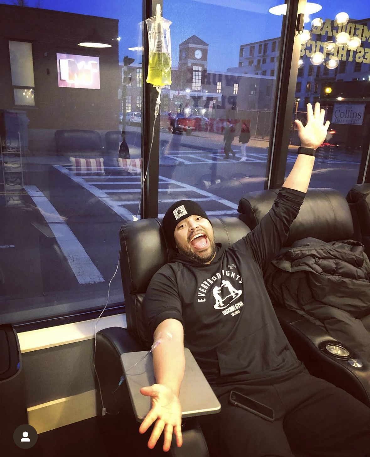 Client celebrating during an evening IV drip session by the clinic's street-facing windows