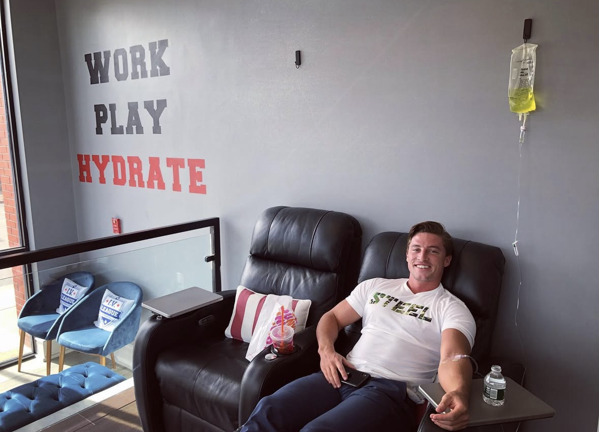 Client smiling during an IV drip beside the Work Play Hydrate wall mural